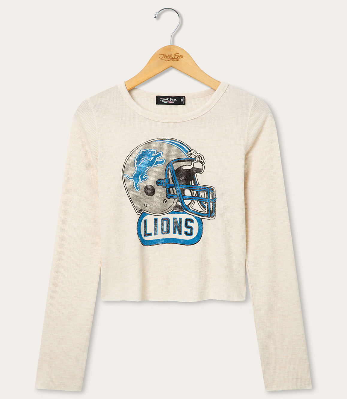 A cream-colored long-sleeved shirt with a distressed Detroit Lions helmet graphic is displayed on a hanger against a plain white background.