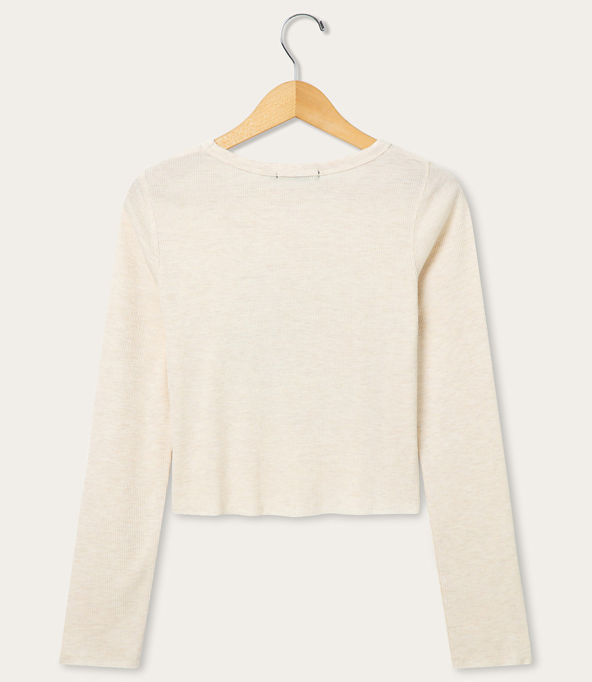 A cream-colored long-sleeved shirt hangs on a wooden hanger against a plain white background.