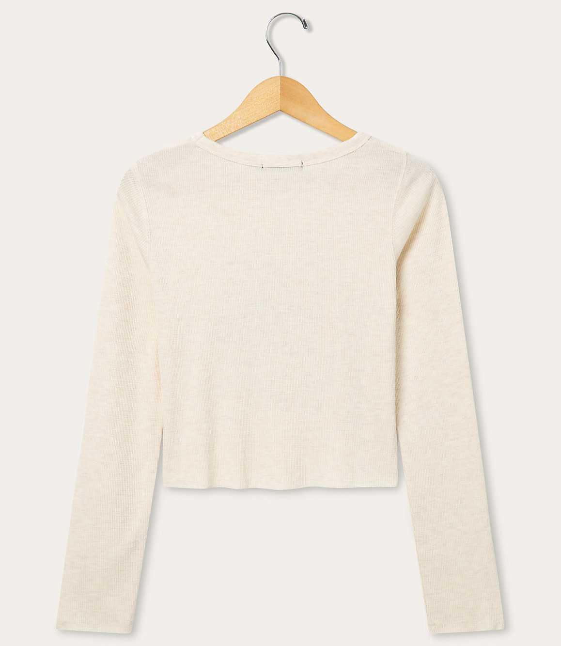 A cream-colored long-sleeved shirt hangs on a wooden hanger against a plain white background.