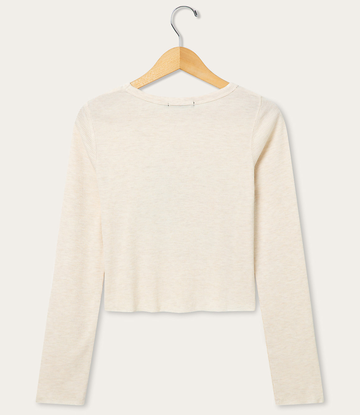 A cream-colored long-sleeved shirt hangs on a wooden hanger against a plain, light-colored background.