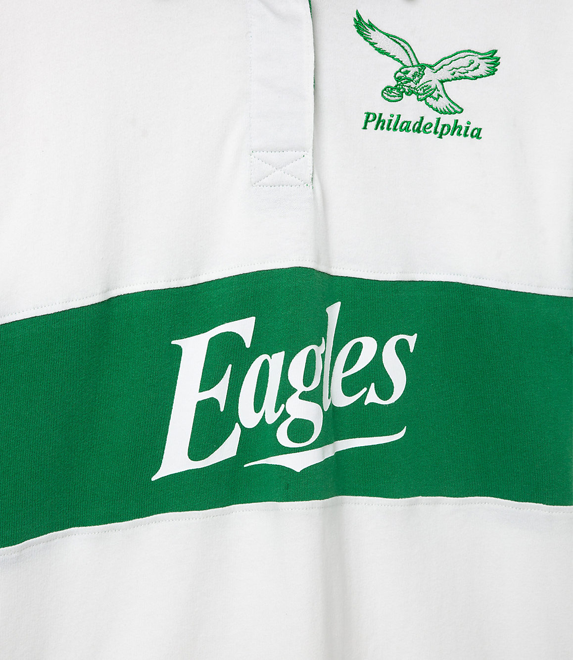 A white rugby shirt with a green stripe across the chest displays "Eagles" in large white lettering, while a green eagle logo and "Philadelphia" are embroidered on the upper right chest.