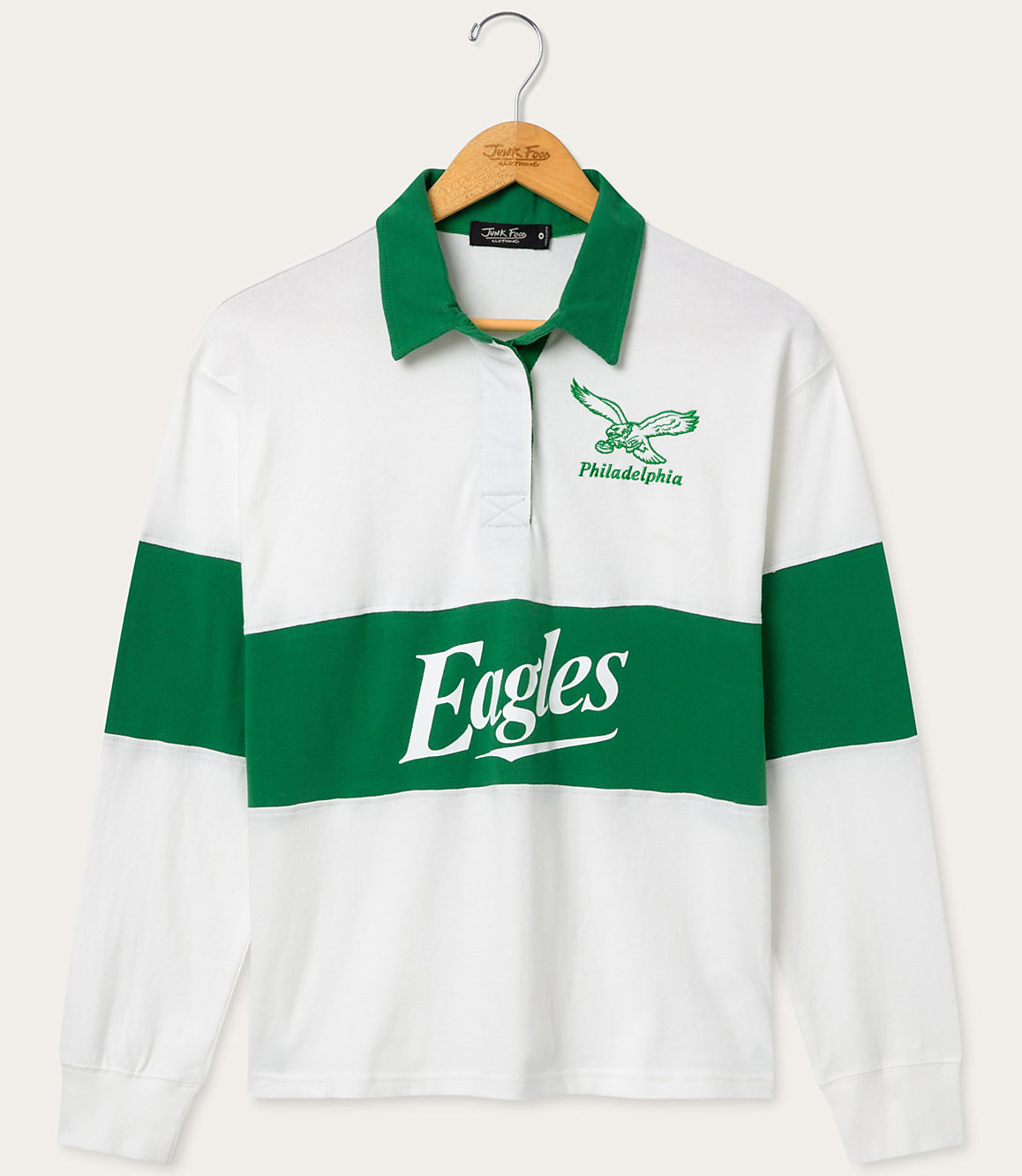 A white and green Philadelphia Eagles rugby shirt hangs on a wooden hanger against a plain white background.
