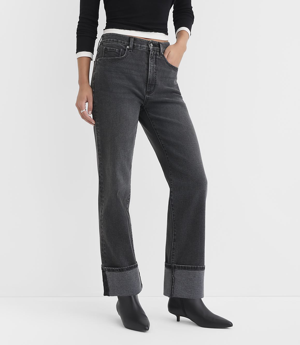 A person in dark wash cuffed jeans and black boots stands against a plain white background.