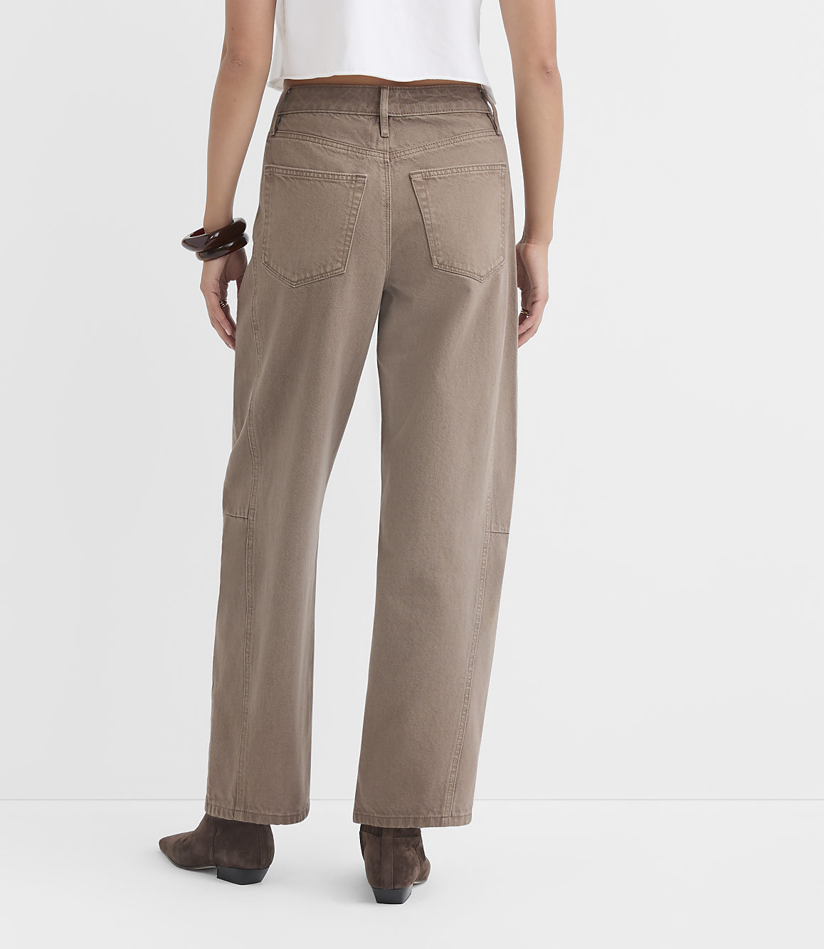 A person wearing loose-fitting brown pants and dark boots stands against a plain white background.