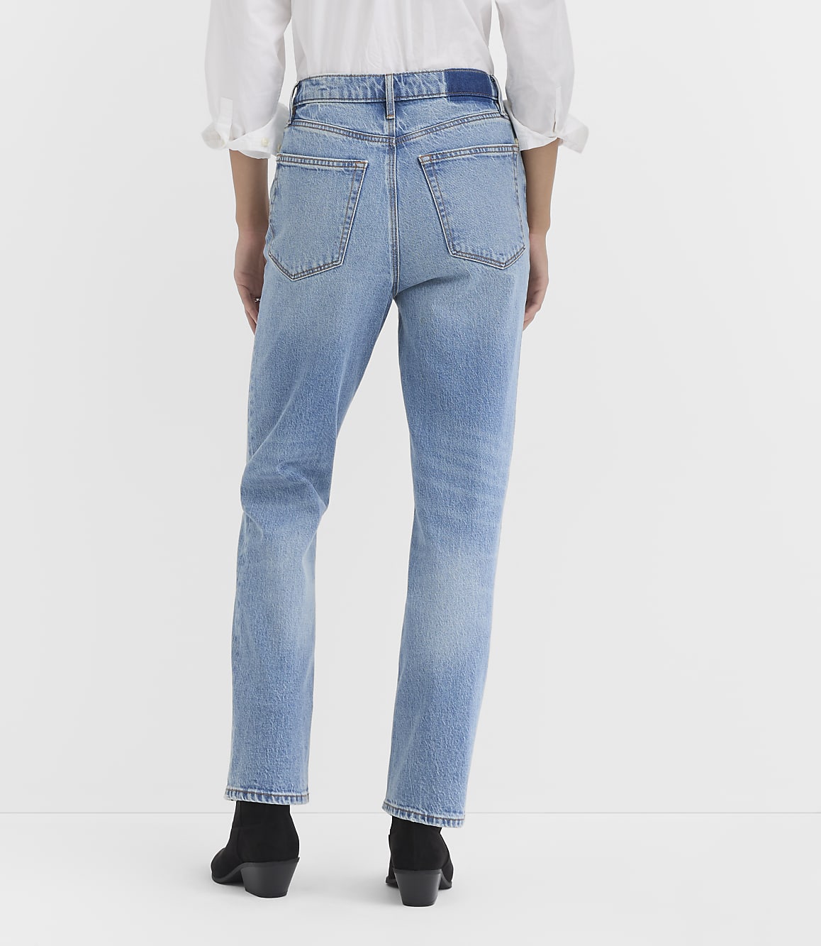 A person wearing light-wash denim jeans and black boots stands against a plain white background.