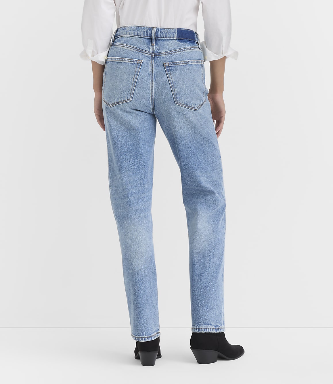 A person wearing light-wash jeans and black boots stands against a plain white background.