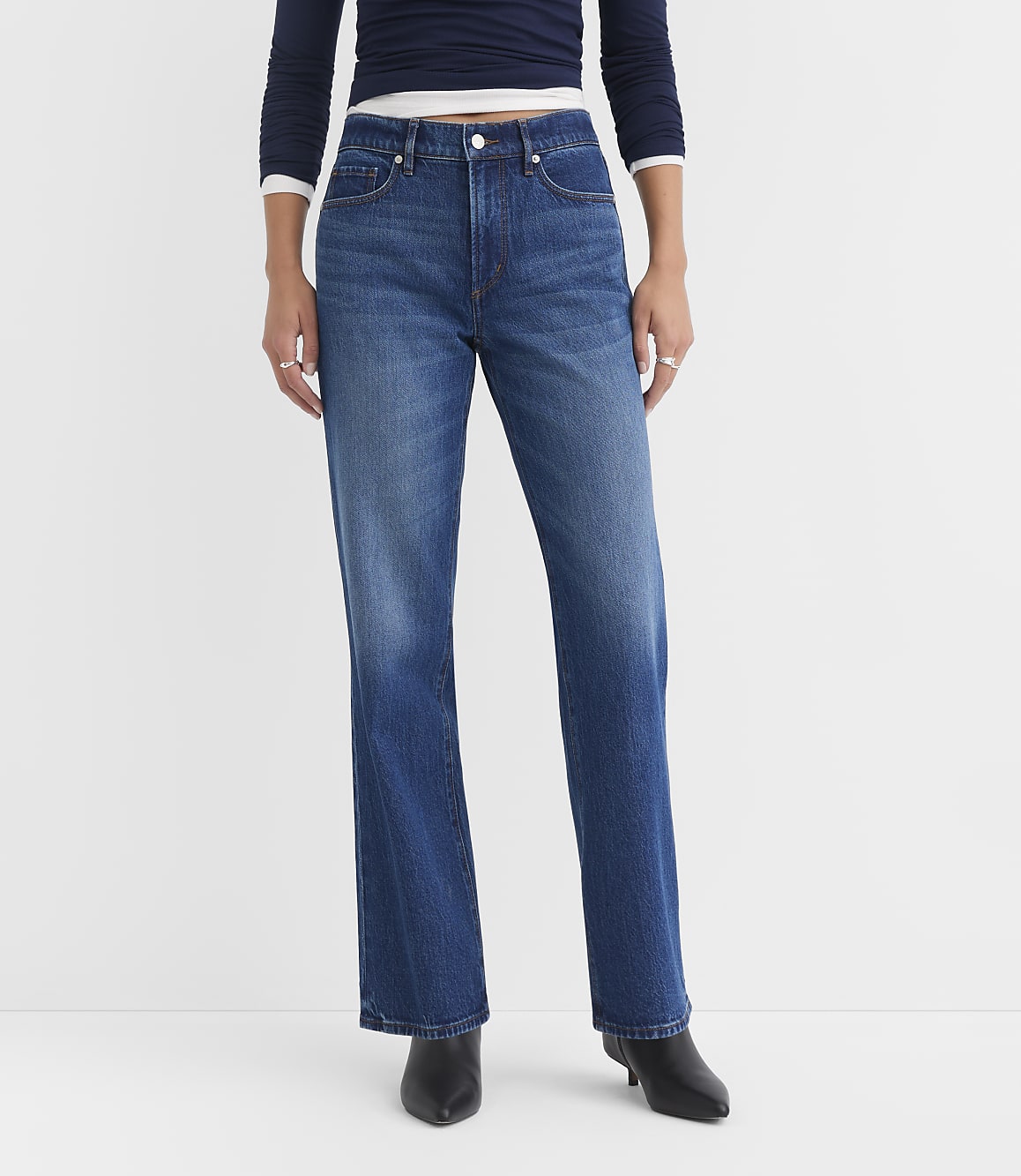 A person wearing dark blue jeans and a navy top stands against a plain white background.
