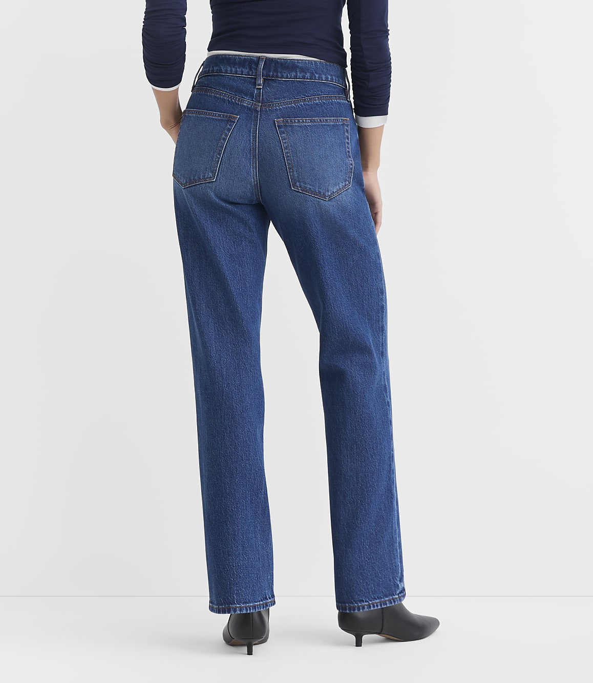 A person wearing blue jeans and black heeled boots stands against a plain white background.
