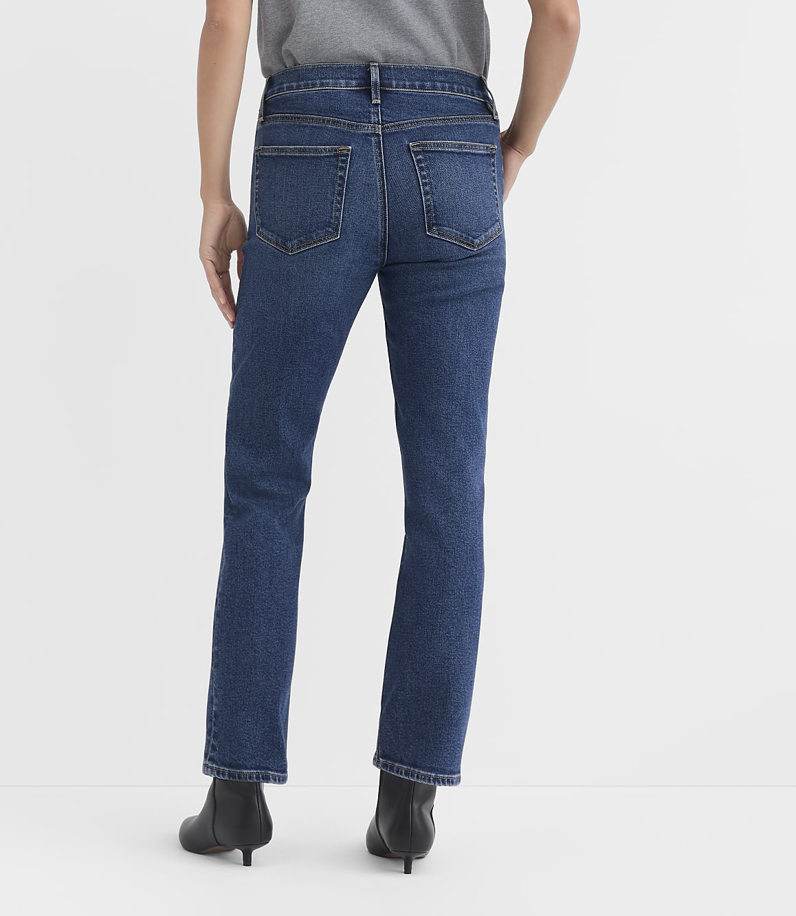 A person wearing dark wash denim jeans and black heeled boots stands against a plain white background.