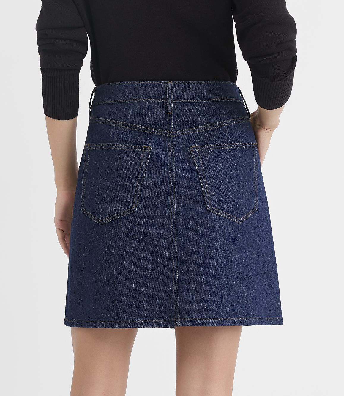 A person wearing a dark blue denim skirt stands against a plain white background.
