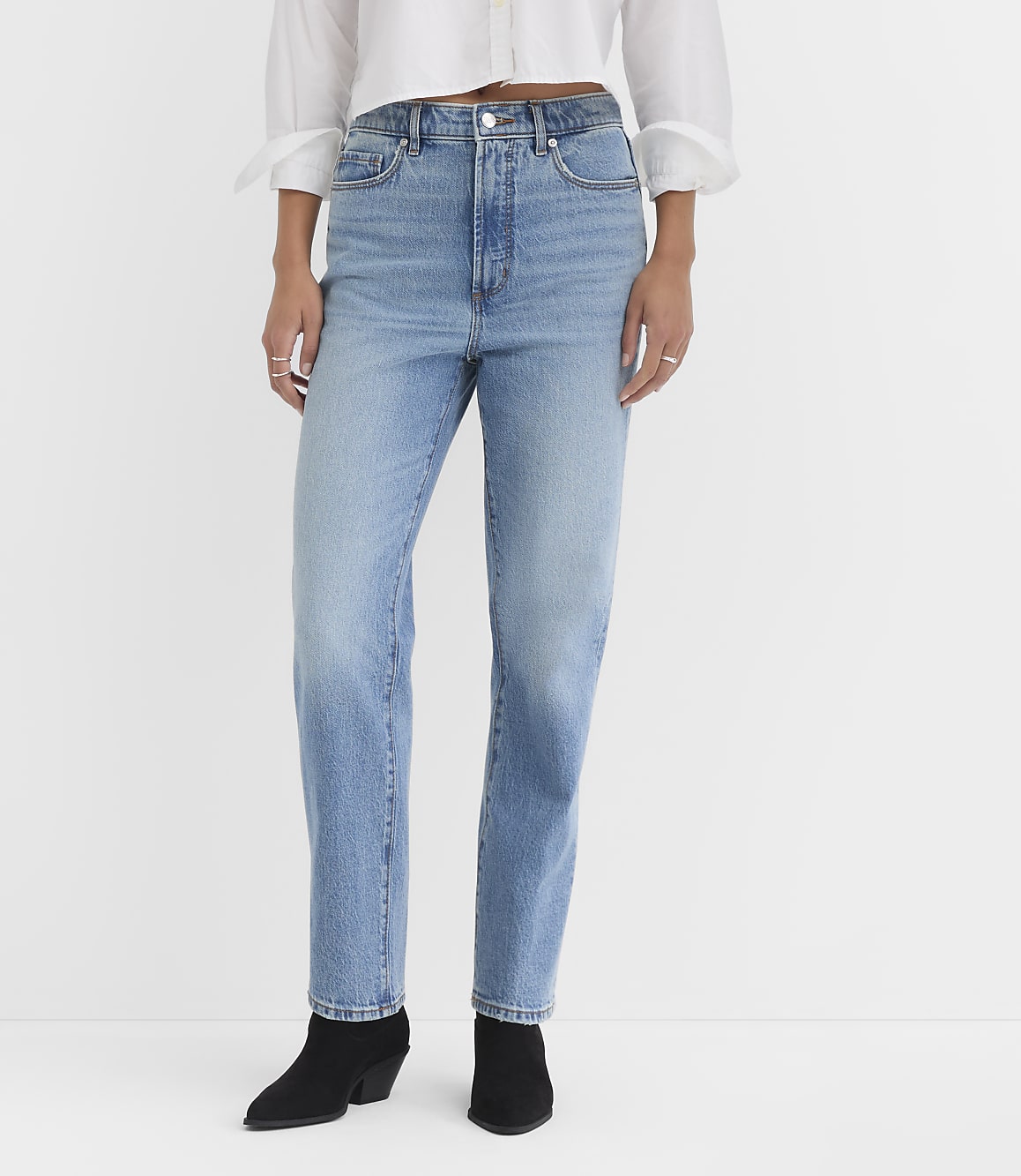 A person wearing light-wash jeans and black boots stands against a plain white background.