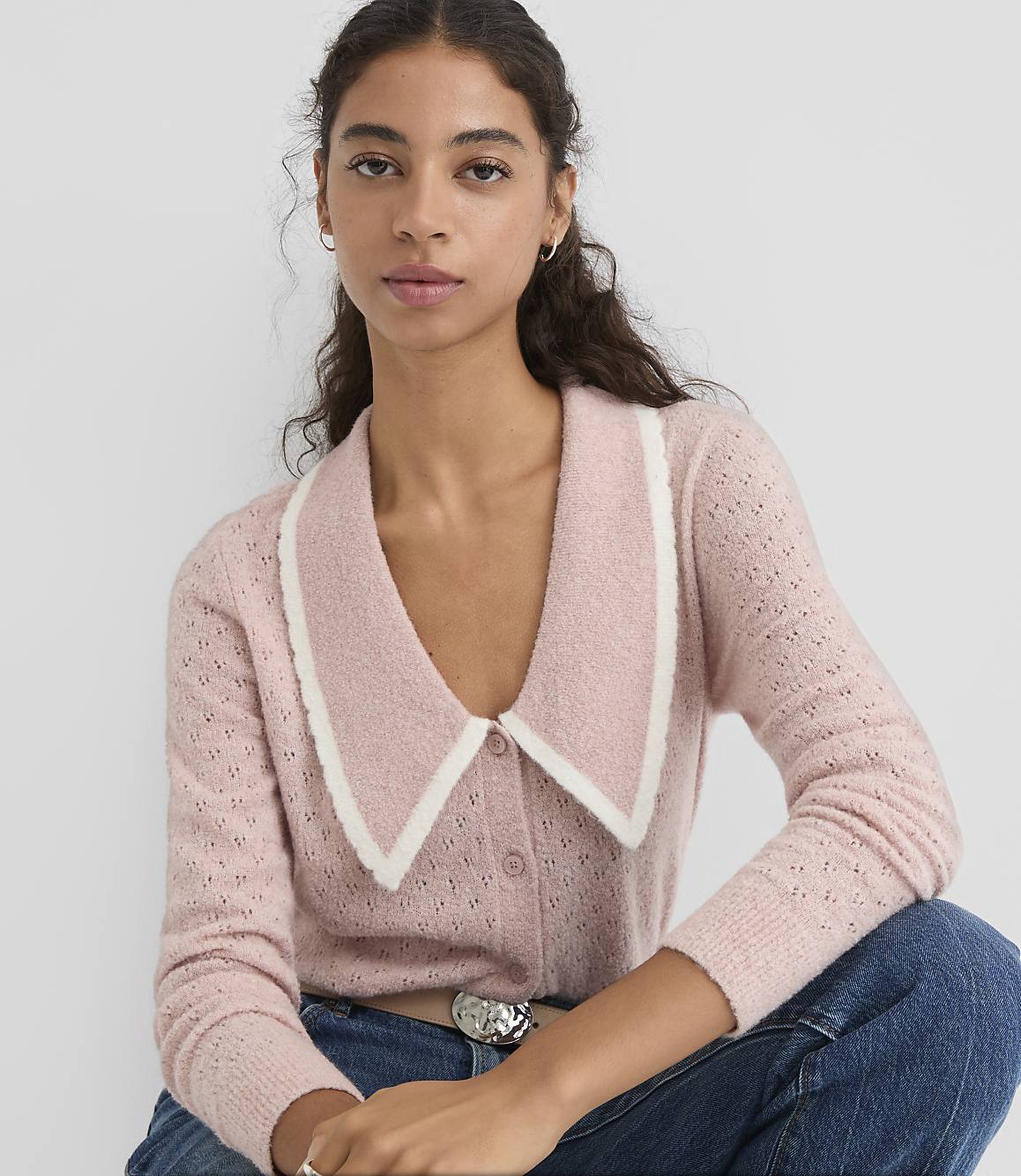 A woman in a pink cardigan with a cream collar poses against a plain white background.