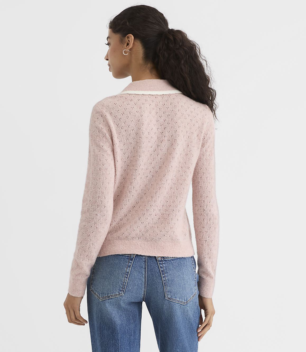 A woman in a pink, textured sweater with a lace collar stands against a plain white background.