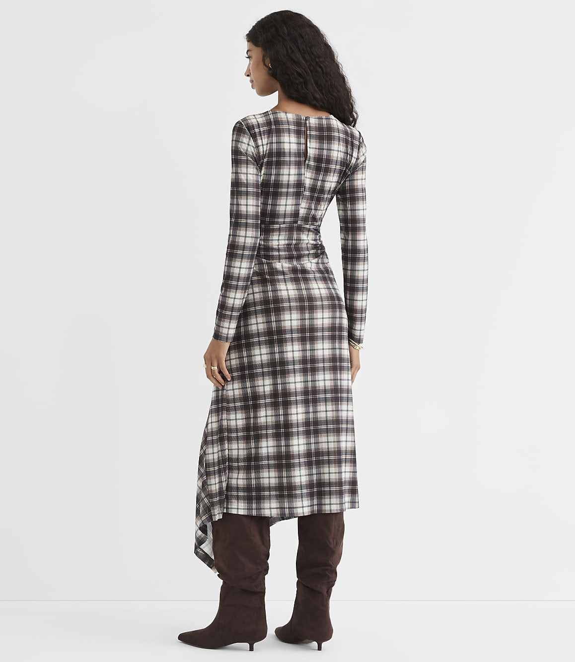 A woman in a plaid dress and brown boots stands against a plain white background.