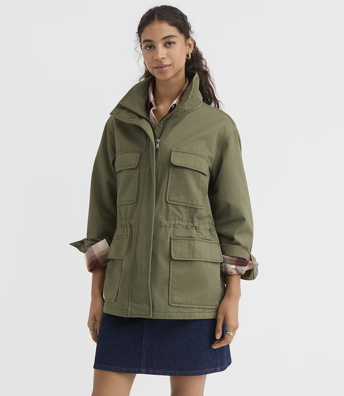 A woman in a green jacket and denim skirt stands against a plain white background.