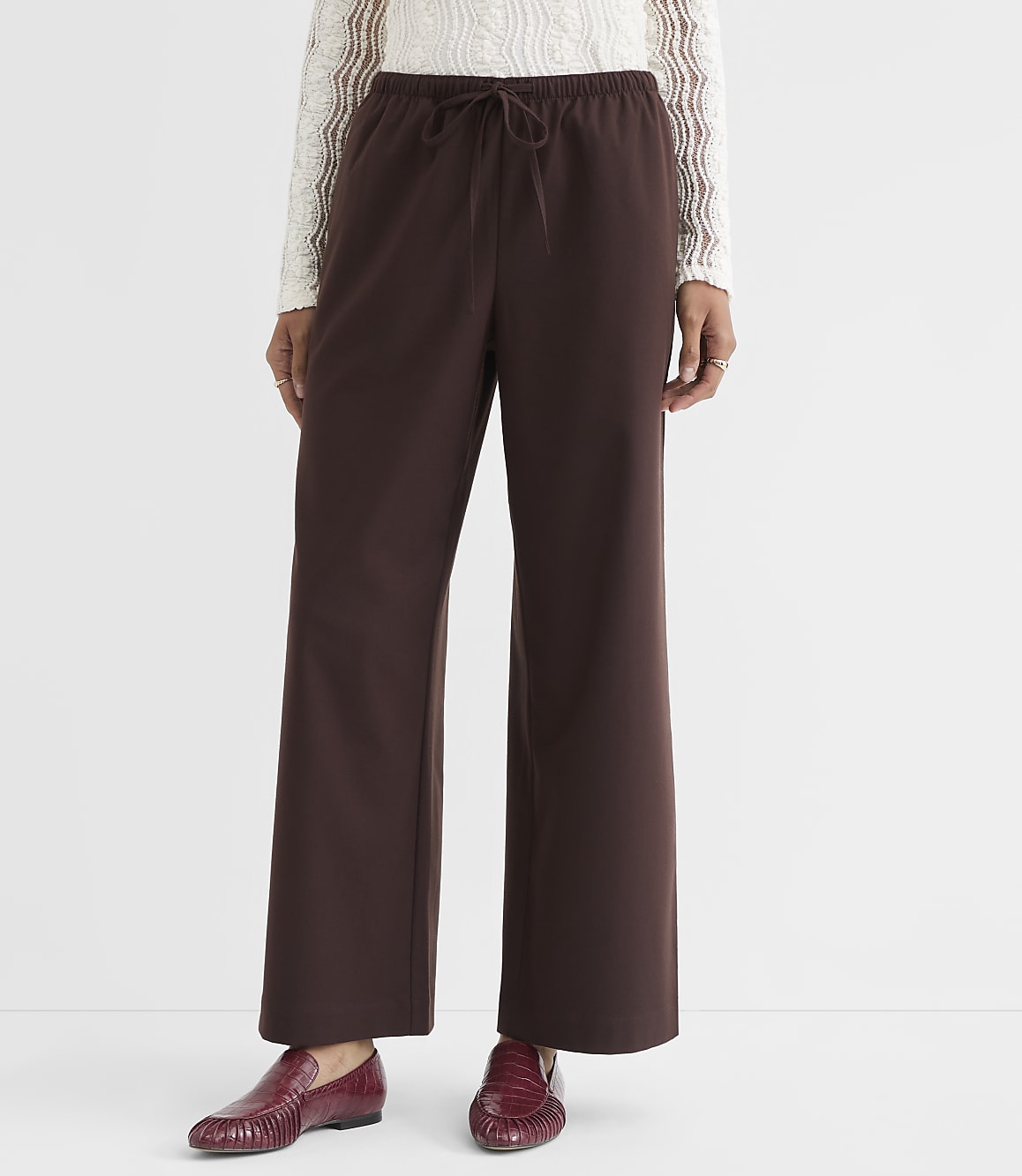 A person stands in brown wide-leg pants and red loafers against a plain white background.