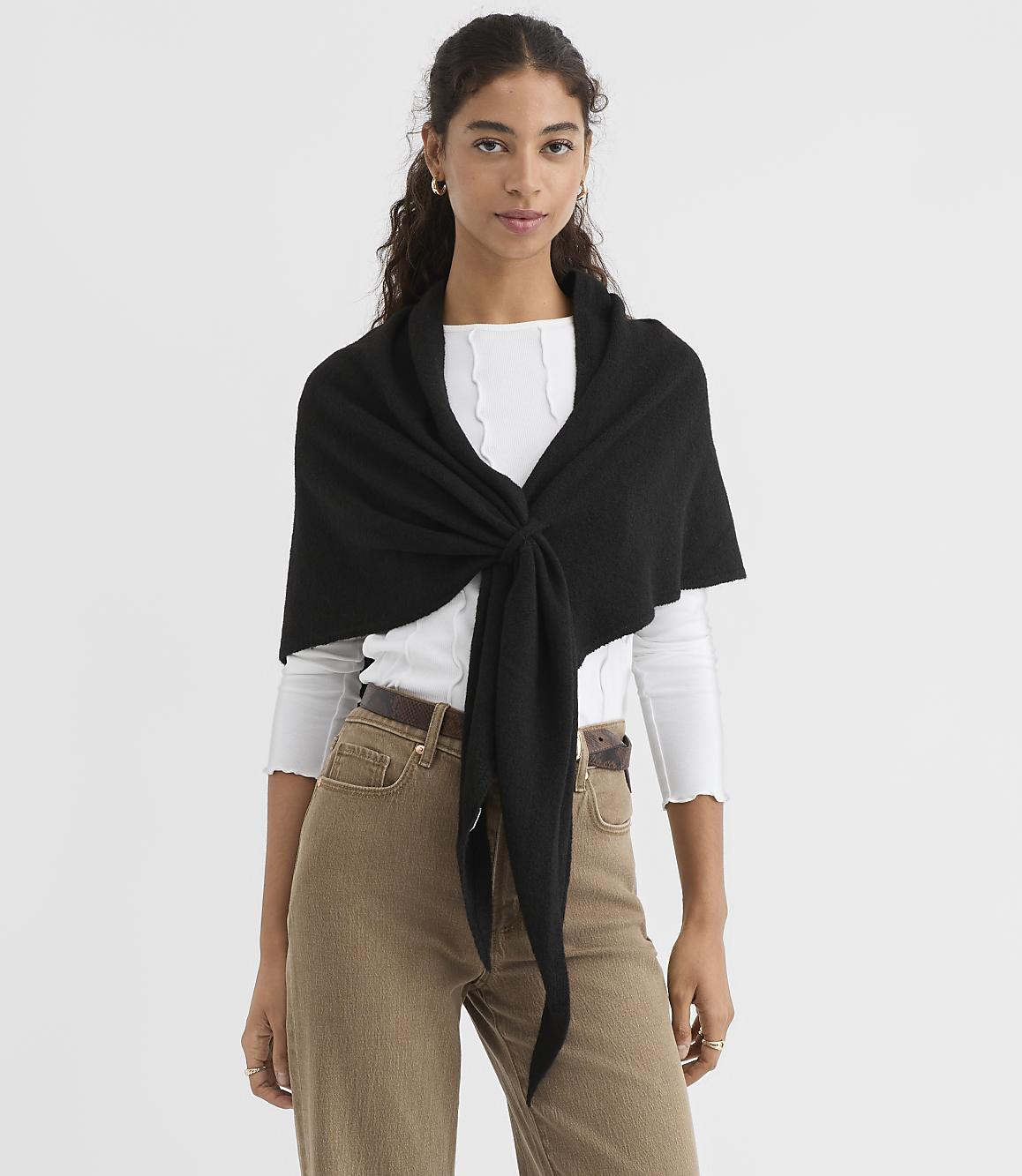A woman in a white top and brown pants models a black shawl tied in front against a plain white background.