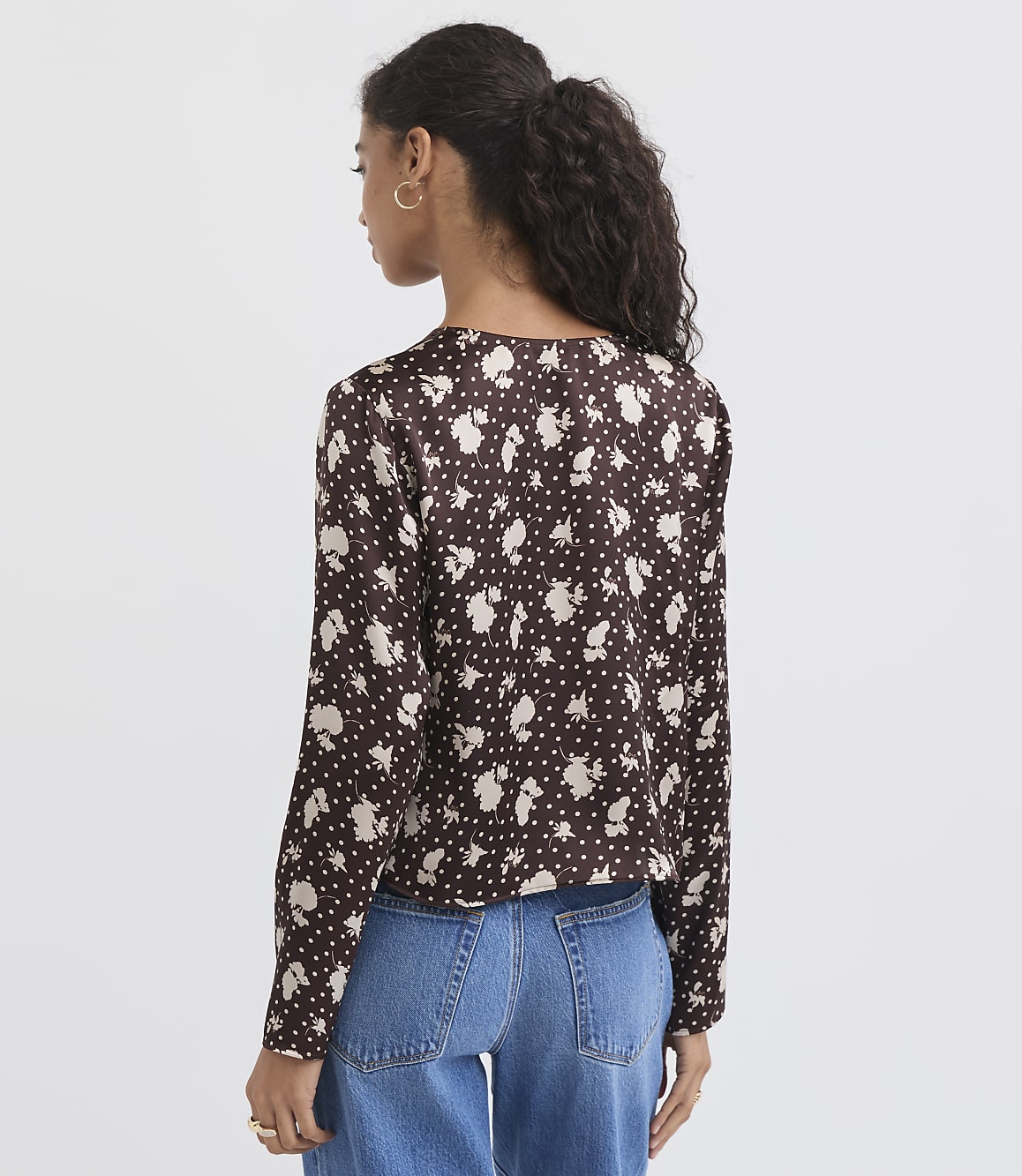 A woman in a floral print blouse and jeans stands against a plain white background.