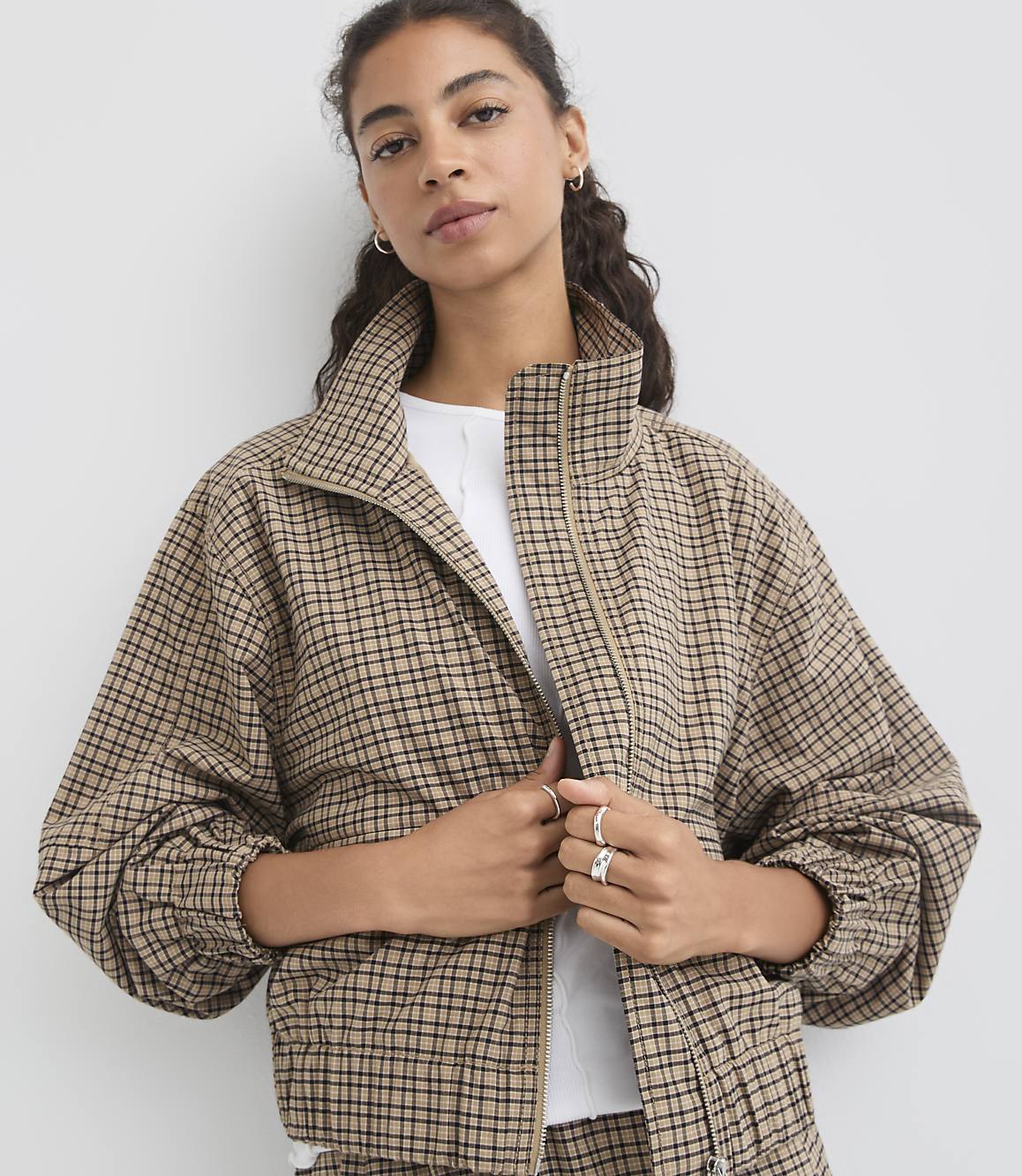 A woman in a plaid jacket stands against a plain white background.