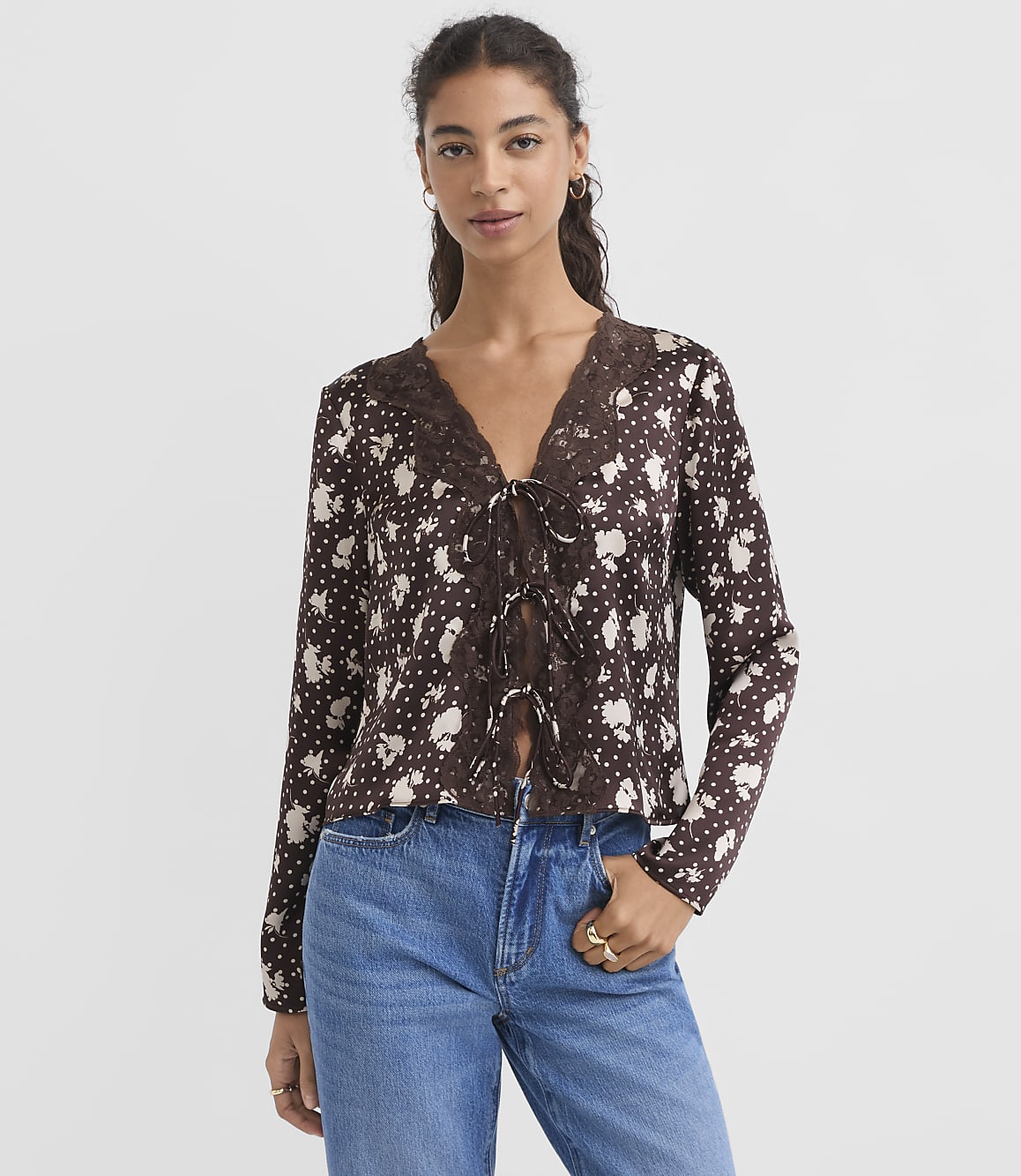 A woman in a floral print top and jeans stands against a plain white background.