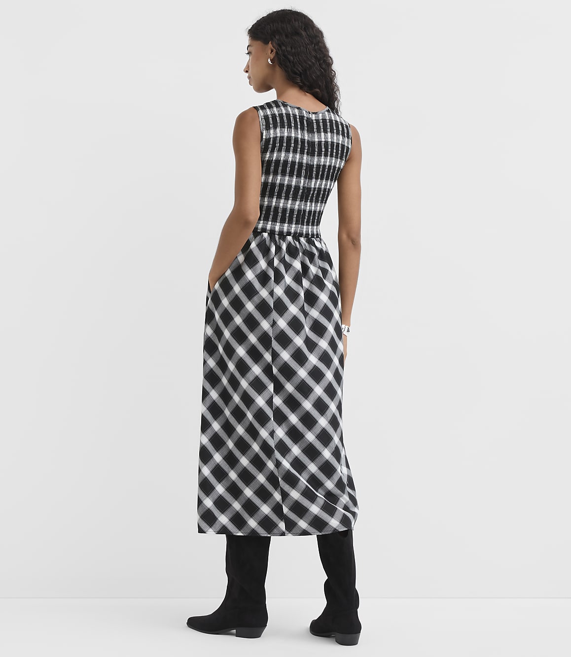A woman in a black and white checkered dress stands against a plain white background.