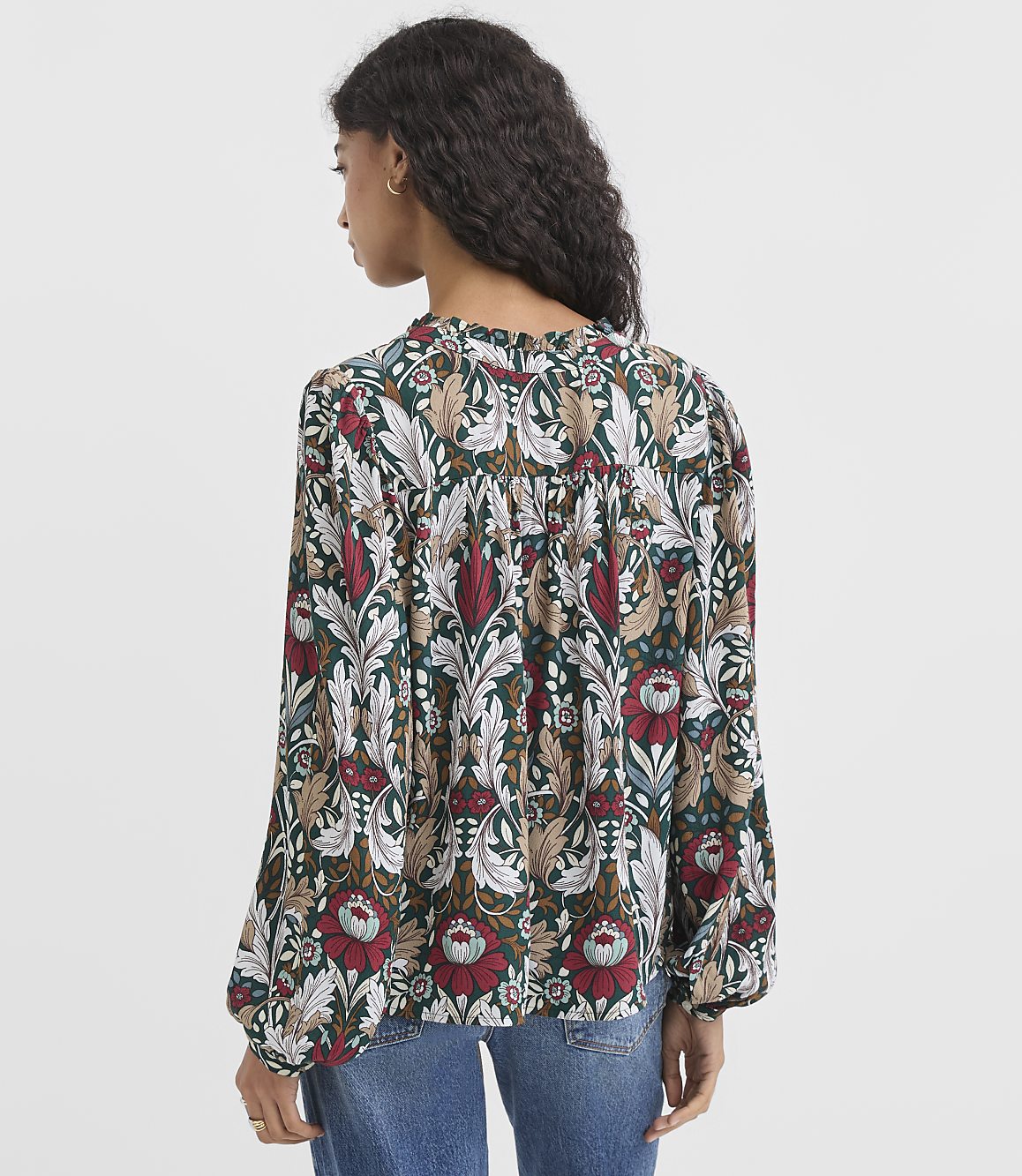 A woman in a patterned blouse stands against a plain white background.
