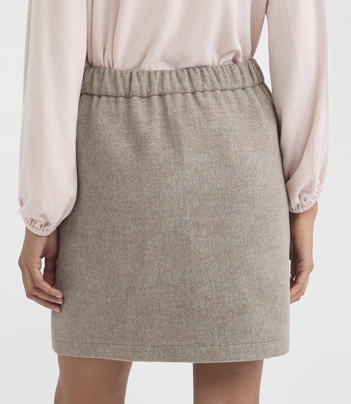 A person in a light pink blouse and a textured brown mini skirt stands against a plain white background.