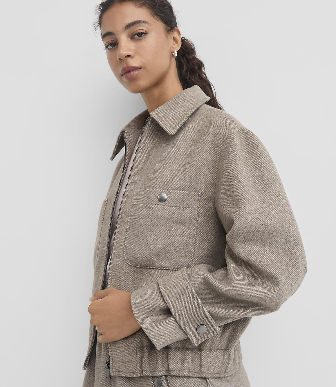 A woman in a textured beige jacket stands against a plain white background.