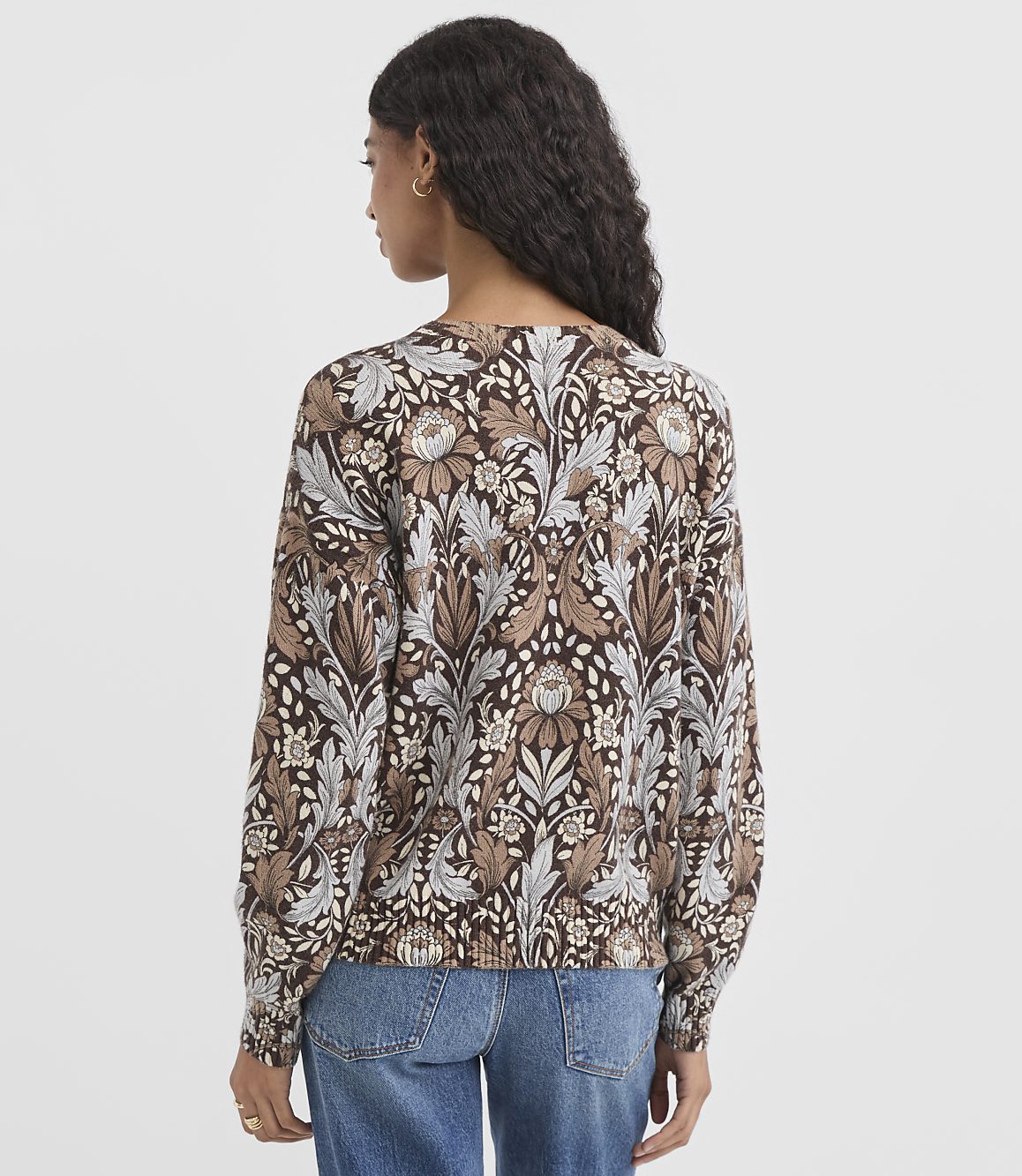 A woman in a patterned sweater and jeans stands against a white background.