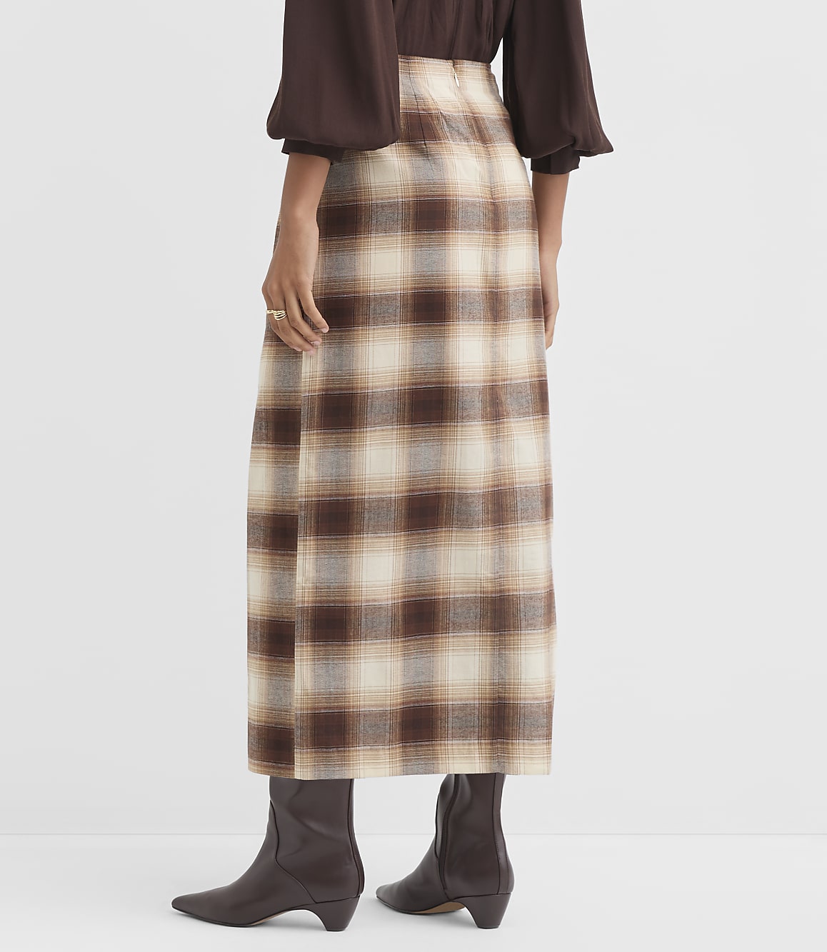 A person stands in a plaid skirt and brown boots against a plain white background.