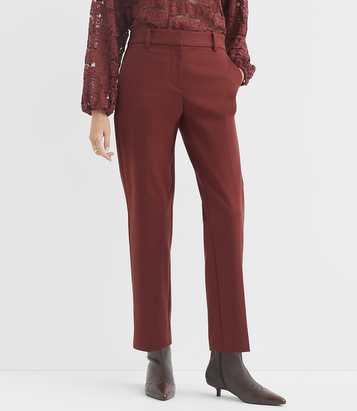 A person in rust-colored pants and a lace top stands against a plain white background.