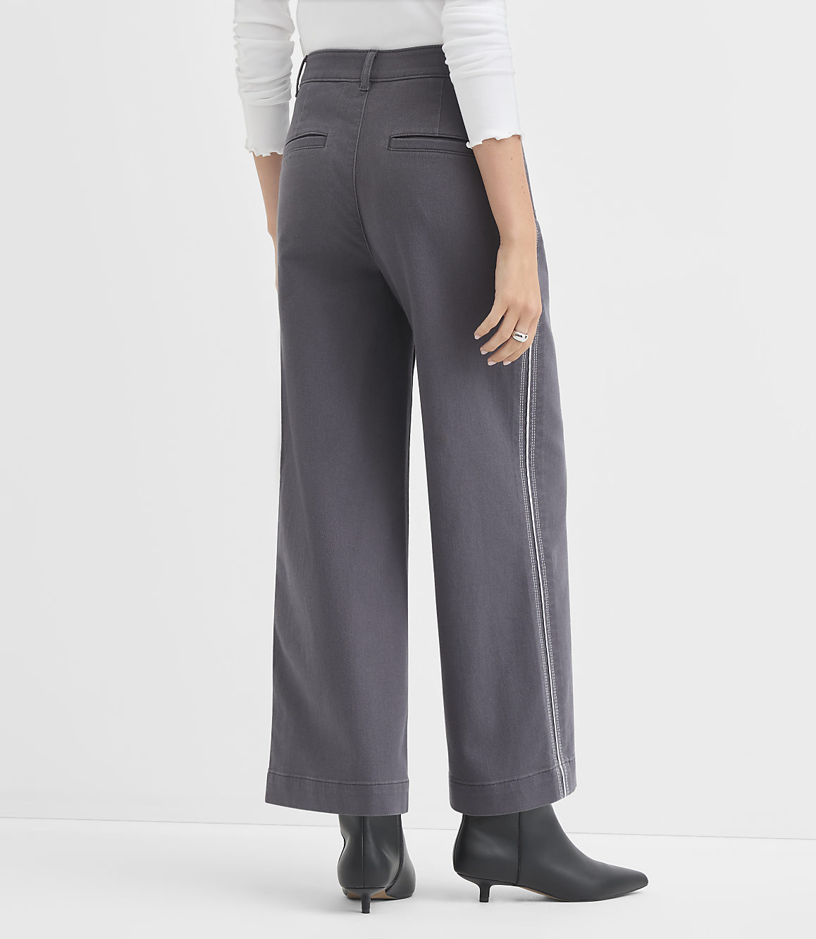 A person wearing wide-leg gray pants with a white stripe down the side and black boots stands against a plain white background.
