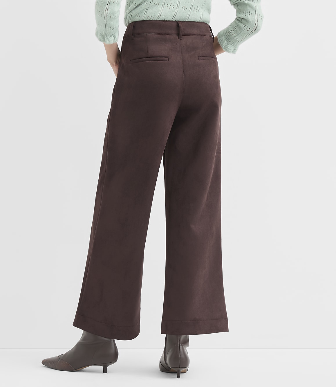 A person wearing brown wide-leg pants and a light green sweater stands against a plain white background.