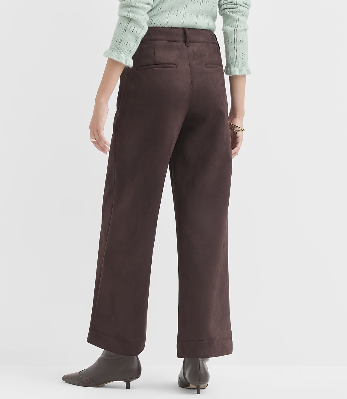 A person wearing brown wide-leg pants and a light green sweater stands against a plain white background.