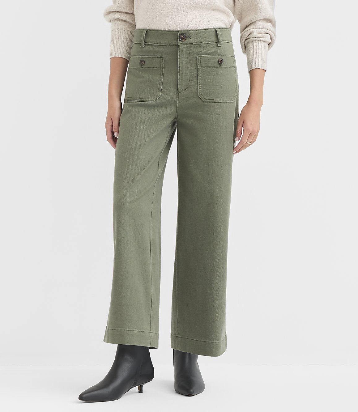 A person stands in the foreground wearing olive green wide-leg pants and black heeled boots, against a plain white background.