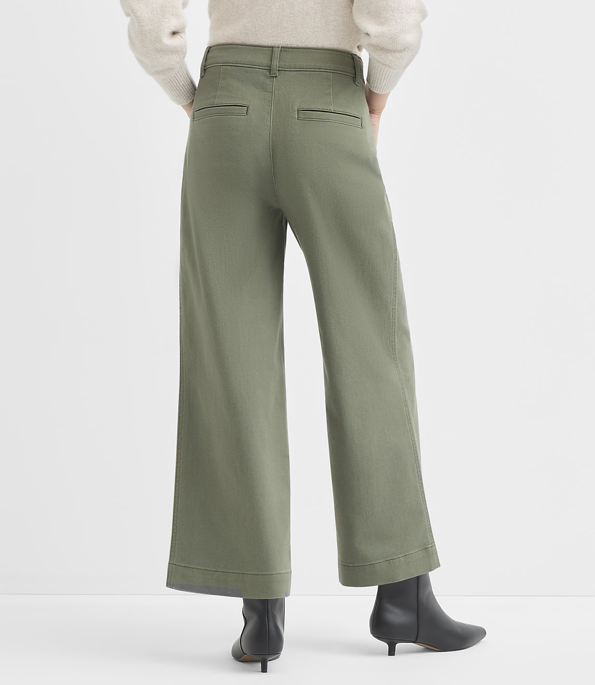 A person wearing olive green wide-leg pants and black boots stands against a plain white background.