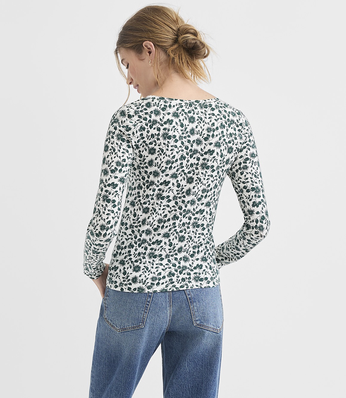 A woman in a floral print top and jeans stands against a plain white background.