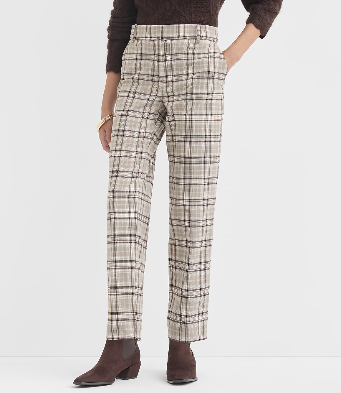 A person stands in the foreground wearing plaid pants and brown boots, against a plain white background.