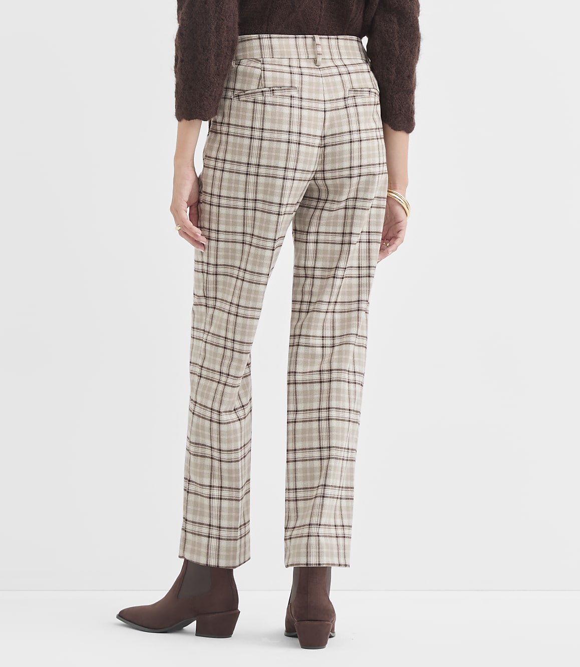 A person wearing plaid pants and brown boots stands against a plain background.