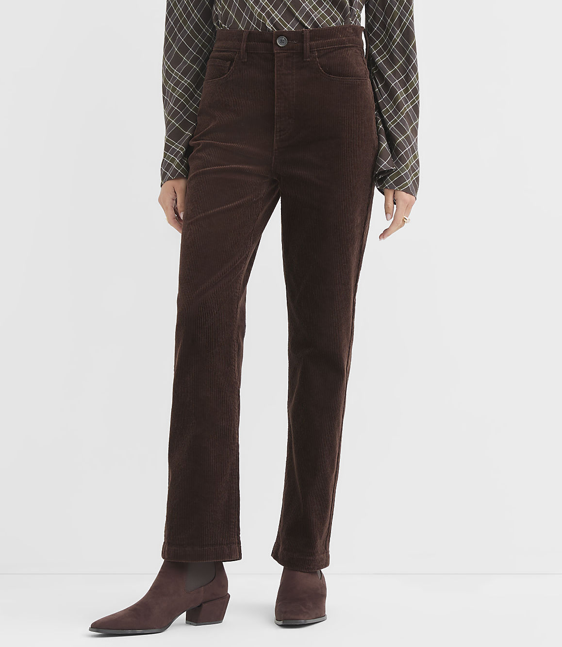 A person wearing brown corduroy pants and a plaid shirt stands against a plain white background.