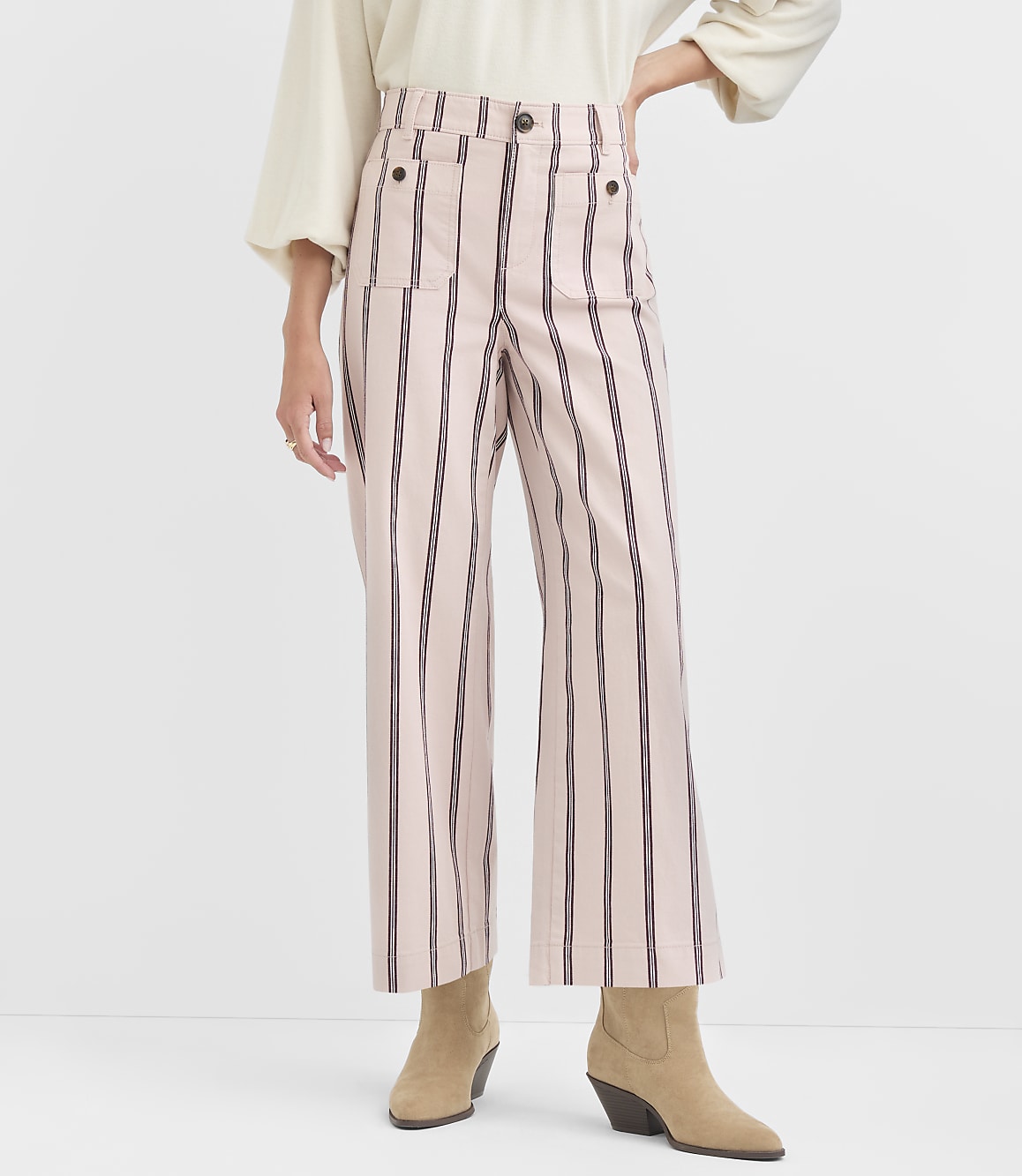 A person stands in front of a plain white background, wearing high-waisted pink and black striped pants and tan ankle boots.