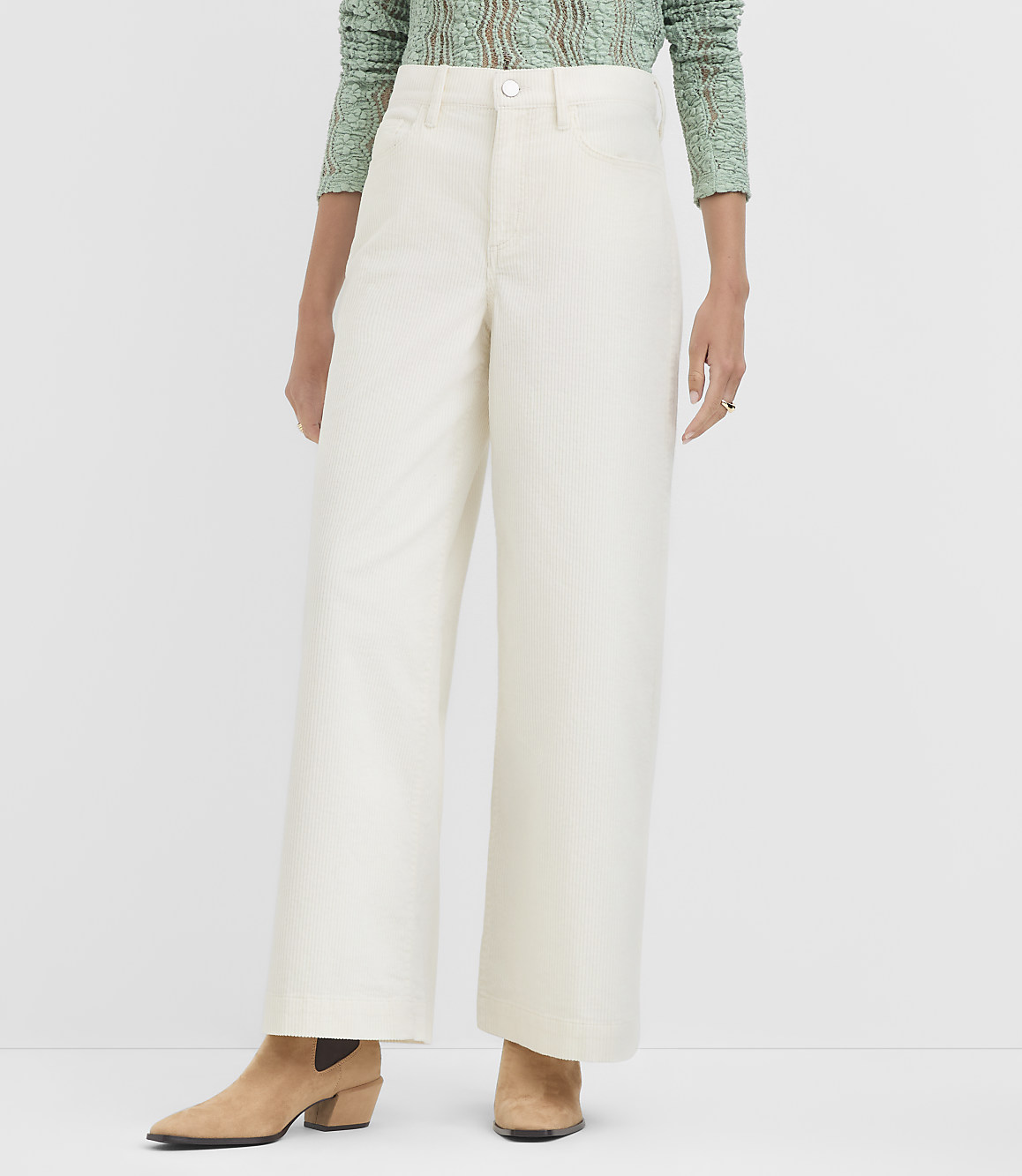 A person stands in cream-colored wide-leg pants and tan boots against a plain white background.