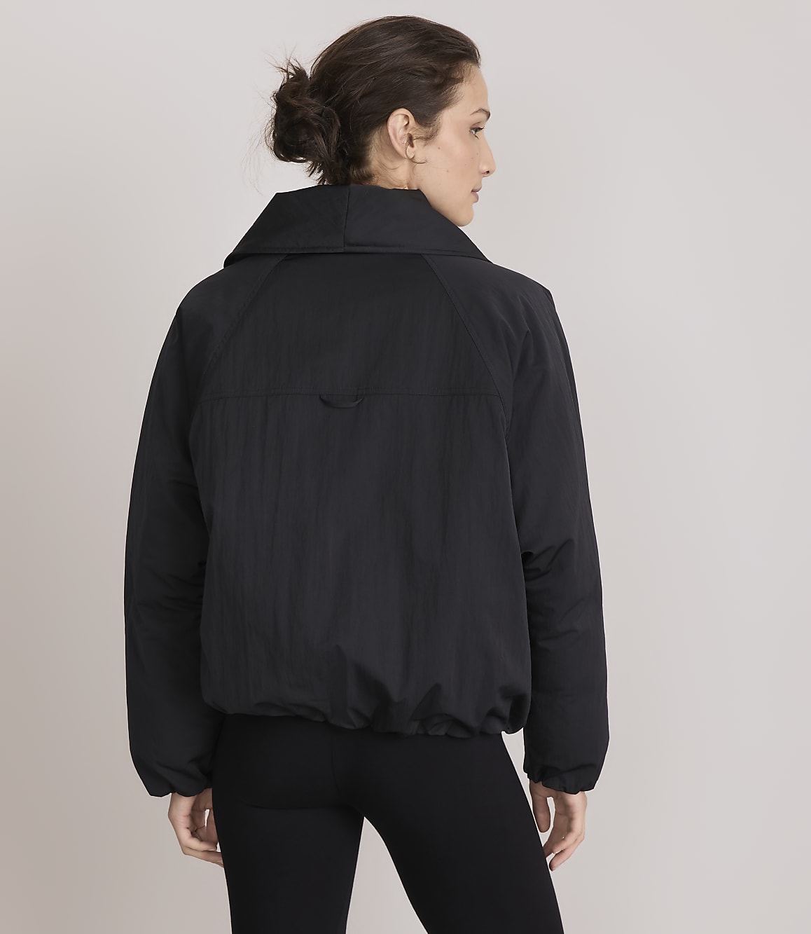 A woman in a black puffer jacket and leggings stands against a plain gray background.