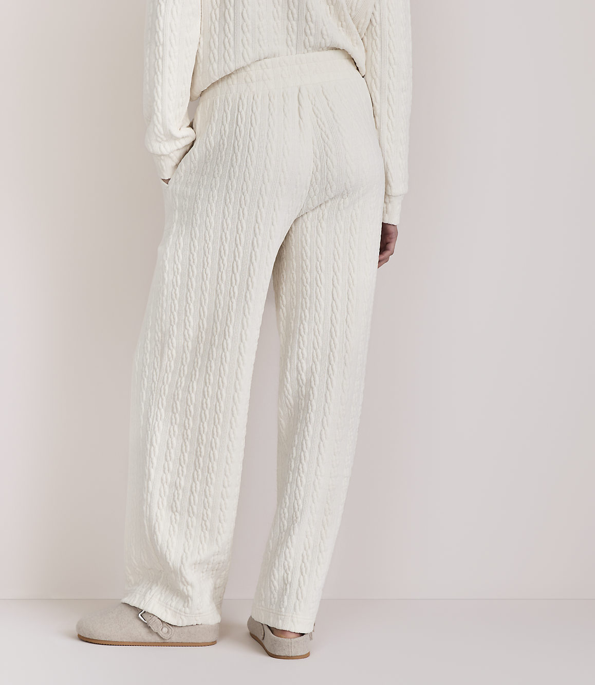 Cream cable-knit pajamas and slippers are shown against a plain, light background.