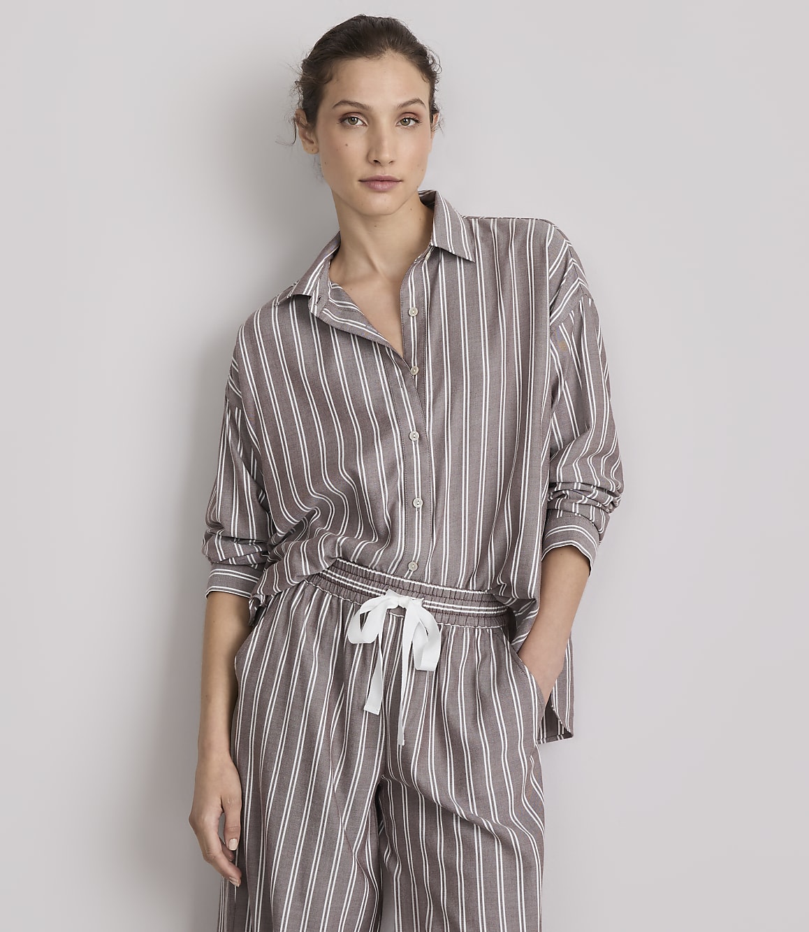 A woman in striped pajamas stands against a plain gray background.