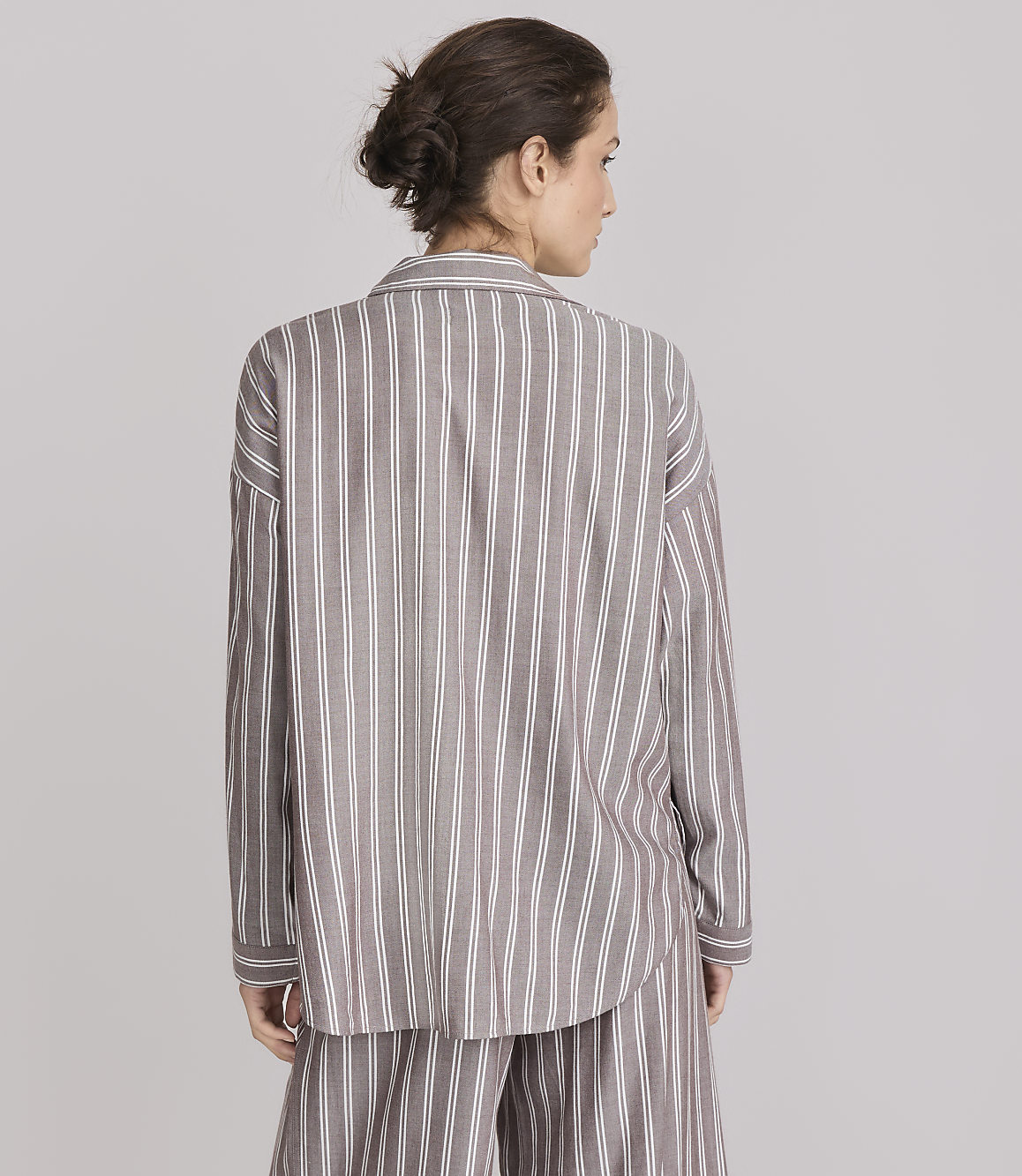 A woman in a striped pajama set stands against a plain gray background.