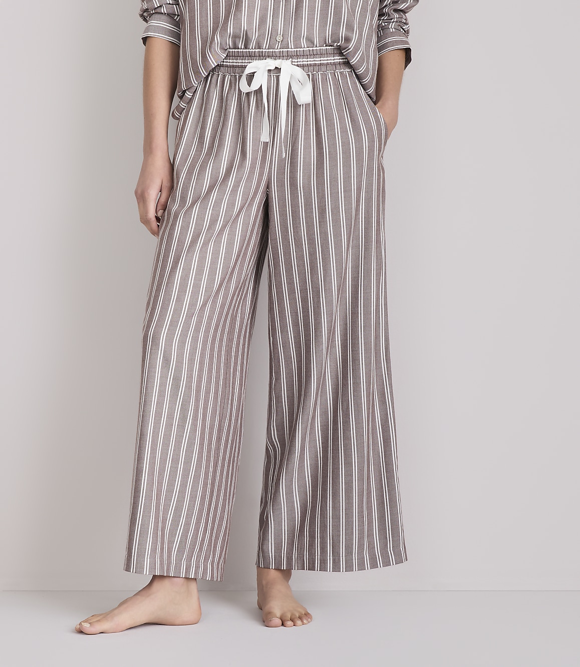 A person stands in striped pajama pants with their hands in their pockets against a plain background.