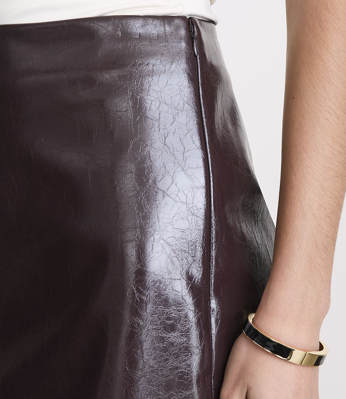 A close-up shot focuses on a shiny, burgundy faux leather skirt with a zipper detail, while a person's arm with a gold and black bracelet is visible on the right.