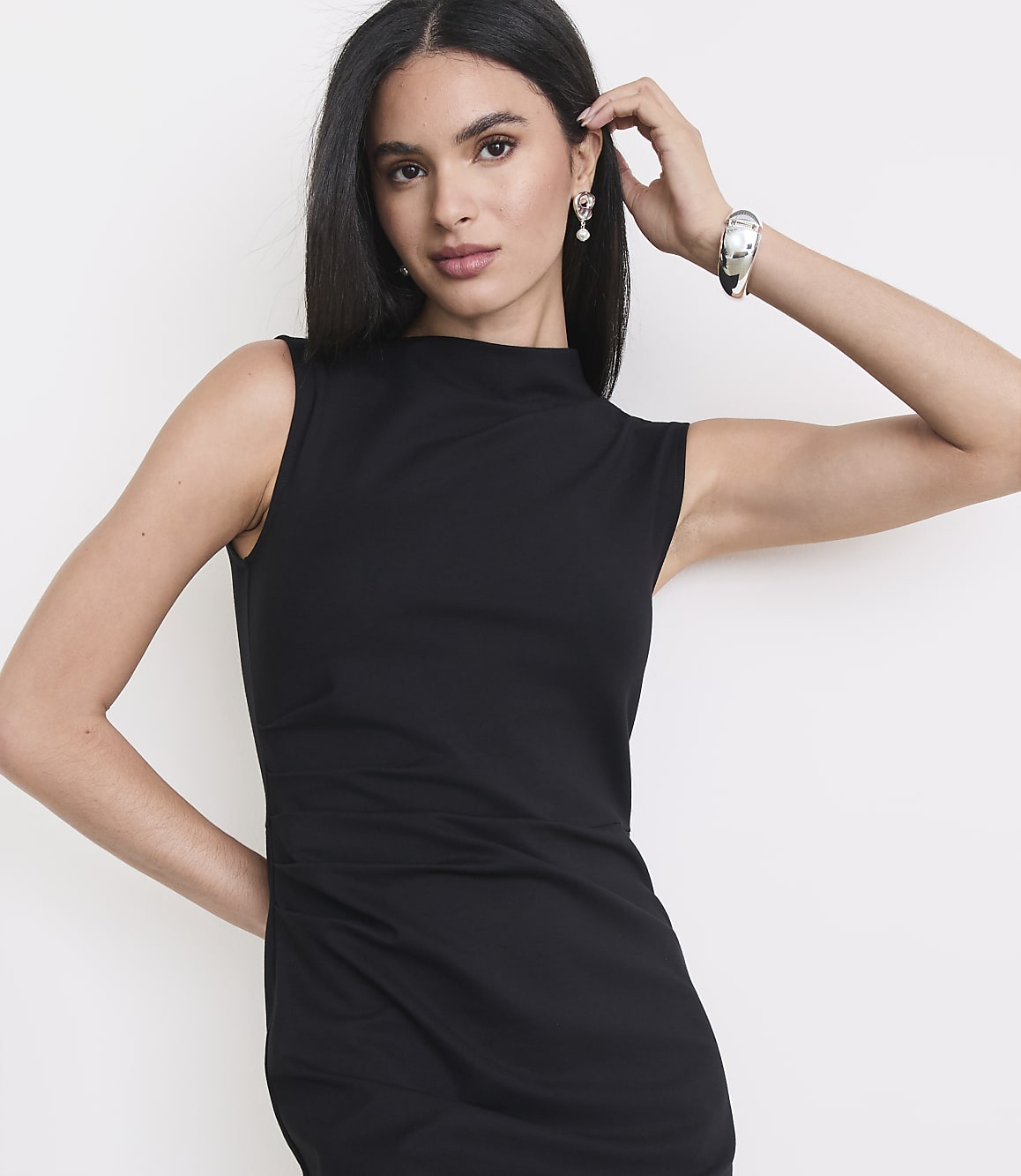 A woman in a black dress poses against a plain white background.