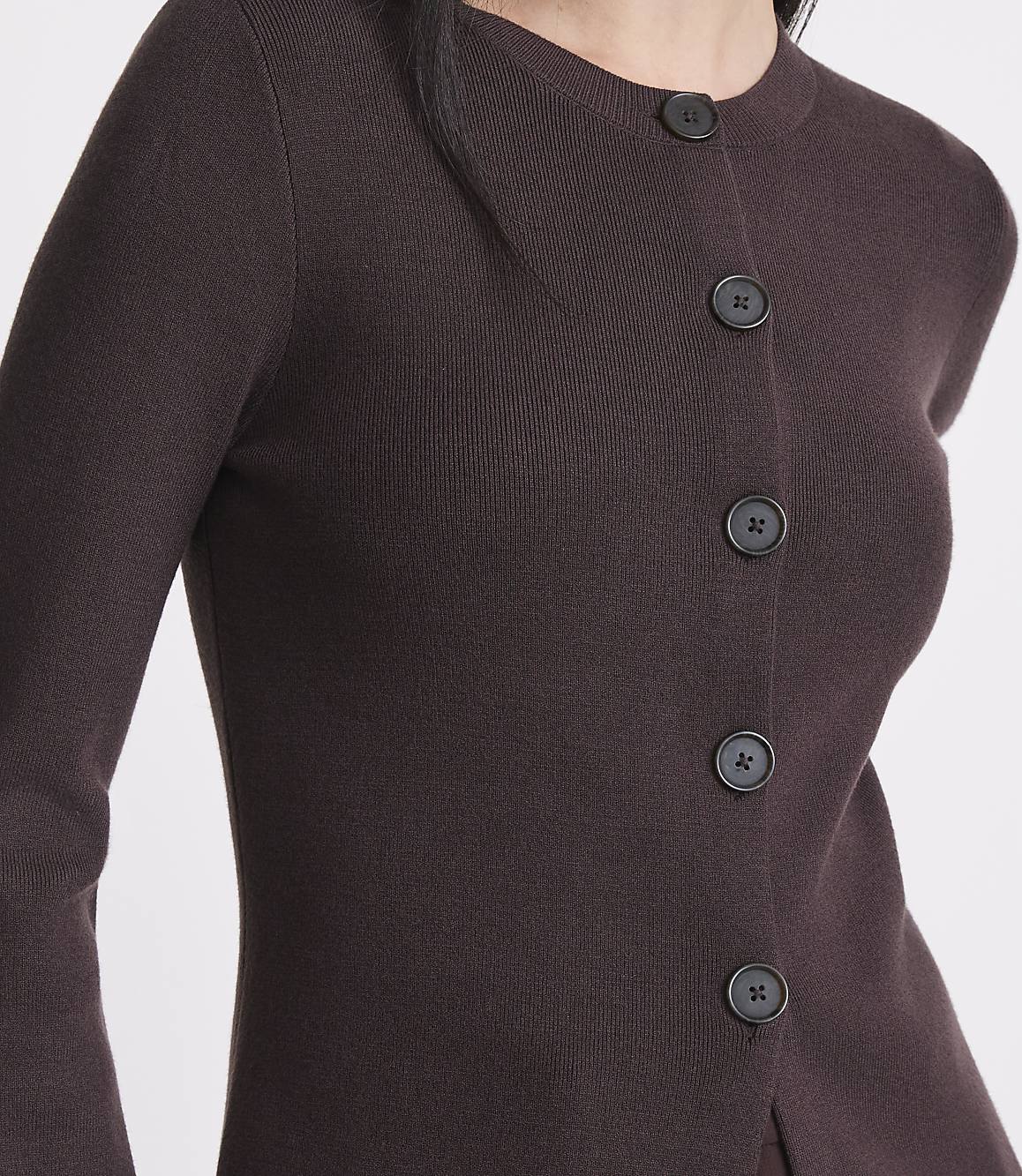 A close-up of a person wearing a dark brown, button-up cardigan with a plain background.
